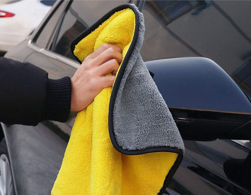 a hand is cleaning the window of a black color car with a silk edge 850 gsm double-sided microfiber towel