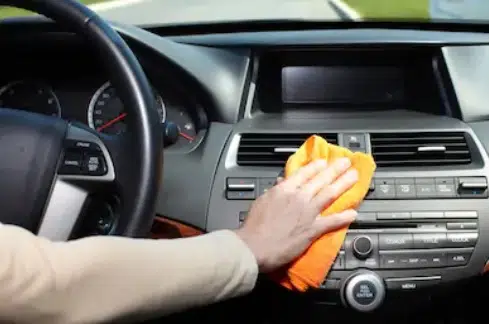 A male hand cleaning car interior and ac vent with a orange colour microfiber cloth