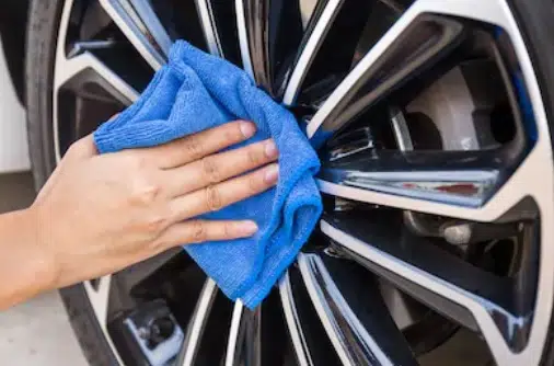 A male hand cleans a tyre rim with a blue microfiber vehicle cleaning cloth