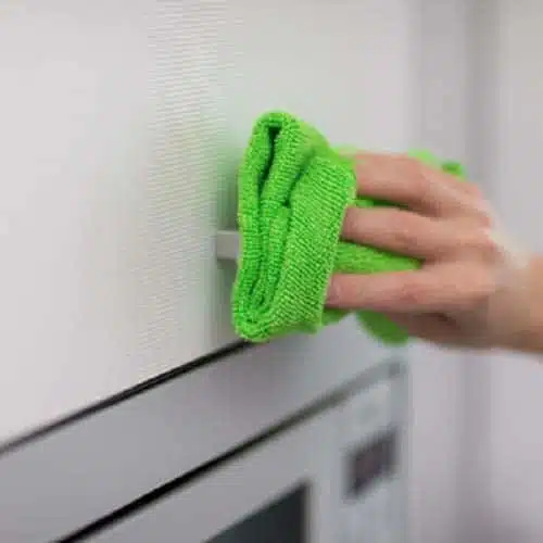 a female hand cleaning fridge with green colour microfiber cleaning cloth